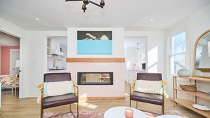 Una sala de estar moderna con dos sillones de cuero, una chimenea, un comedor y un ventanal amplio.