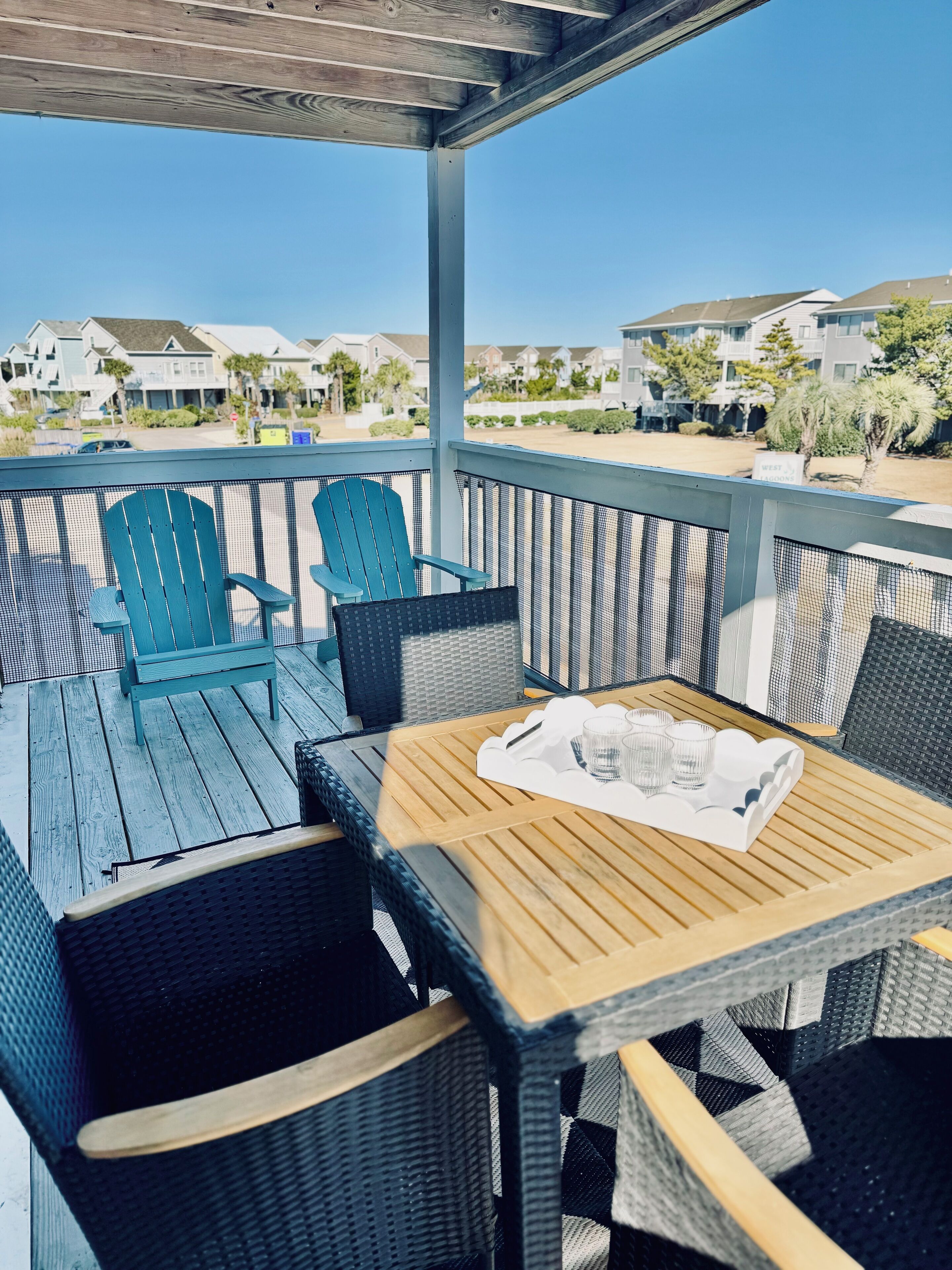 A covered outdoor seating area with wicker furniture and a wooden table, overlooking a residential neighborhood.