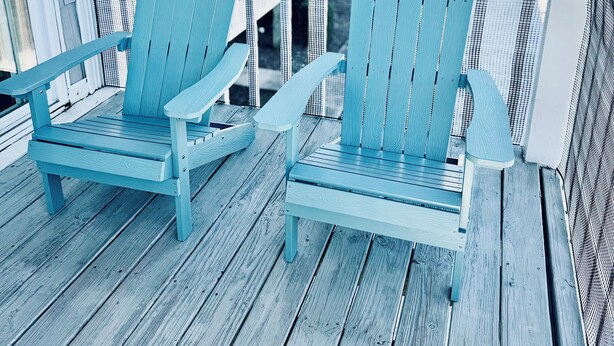 A wooden deck with two Adirondack chairs and a view of a residential area. - Modern, luxurious 1-bedroom condo in stunning Ocean Isle Beach (Ocean Isle Beach)