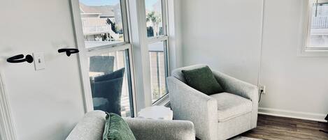 A modern living room with two grey armchairs, a green throw pillow, and a neon sign on the wall.