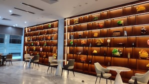 A modern lobby with a marble floor, seating area with round tables and chairs, and a wall decorated with various decorative items. - Royal International Hotel (Georgetown)