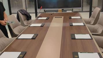 A conference room with a long table, beige chairs, and a large flat-screen TV at the front.