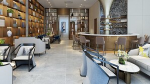 A modern bar area with a curved counter, seating with cushioned chairs, and a wall with shelves displaying books and decorative items. - Royal International Hotel (Georgetown)