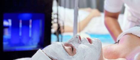 A person lying on a bed with a white sheet, receiving a facial treatment.