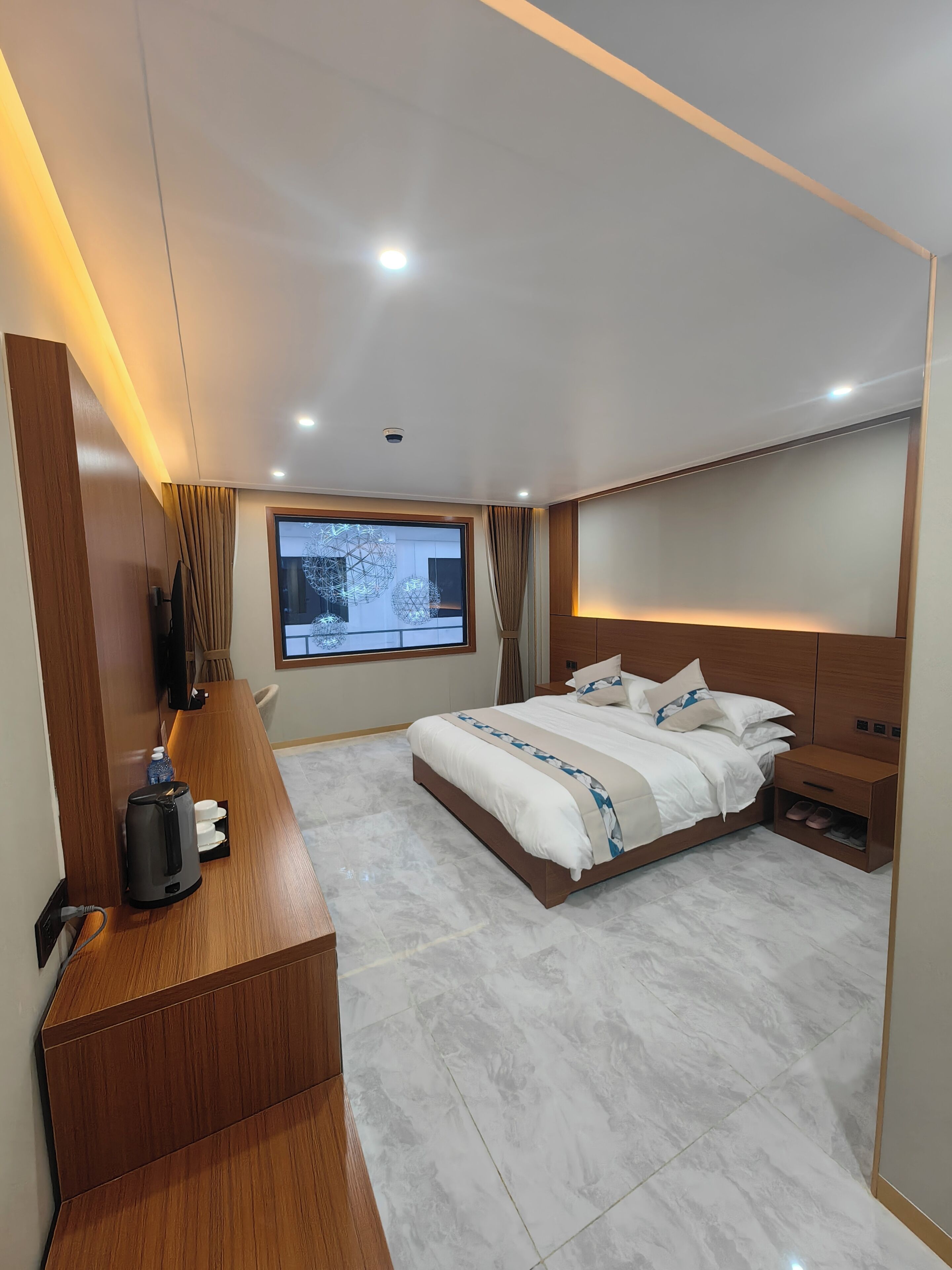 Une chambre moderne avec un grand lit, un bureau en bois, une télévision et une vue sur l’extérieur.