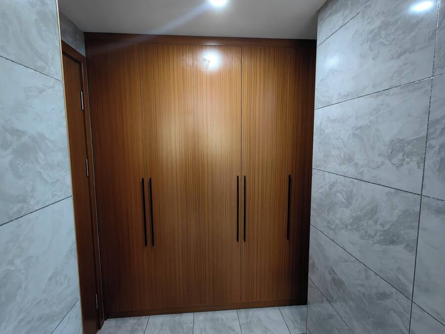 A room with a wooden wardrobe, white marble tiles, and a recessed ceiling light.