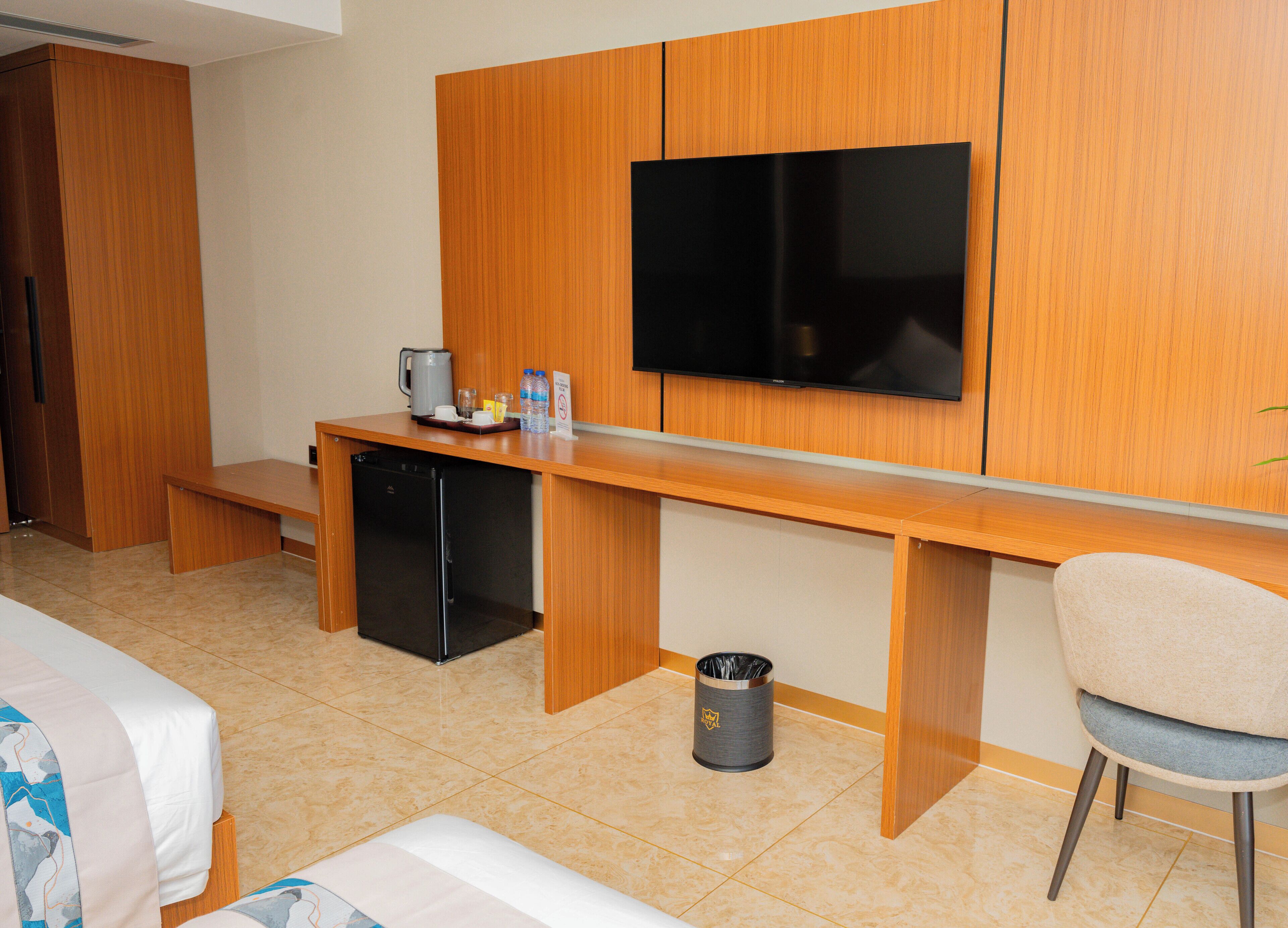 A hotel room with a wooden desk, a television, a mini-fridge, a trash can, and a bed.