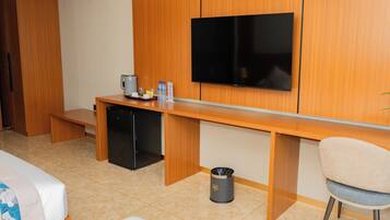 A hotel room with a wooden desk, a television, a mini-fridge, a trash can, and a bed.