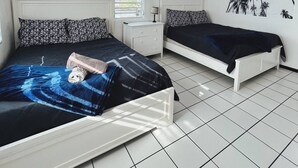 Un dormitorio con dos camas, una mesita de noche, un ventilador de techo y una pared decorada con motivos florales.
