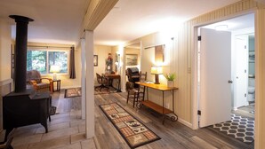 A cozy living room with a fireplace, a dining area, and a hallway leading to a door. - Up-River House on the McKenzie River  (Mckenzie Bridge)