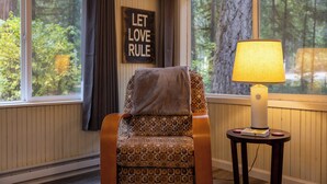 A cozy room with a patterned armchair, a lamp, and a 'LET LOVE RULE' sign. - Up-River House on the McKenzie River  (Mckenzie Bridge)