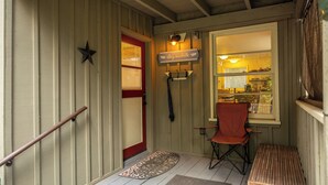A wooden porch with a red door, a bench, a folding chair, and a welcome mat. - Up-River House on the McKenzie River  (Mckenzie Bridge)