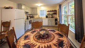 A compact kitchen with white cabinets, a refrigerator, a microwave, and a dining area with a round table and chairs. - Up-River House on the McKenzie River  (Mckenzie Bridge)