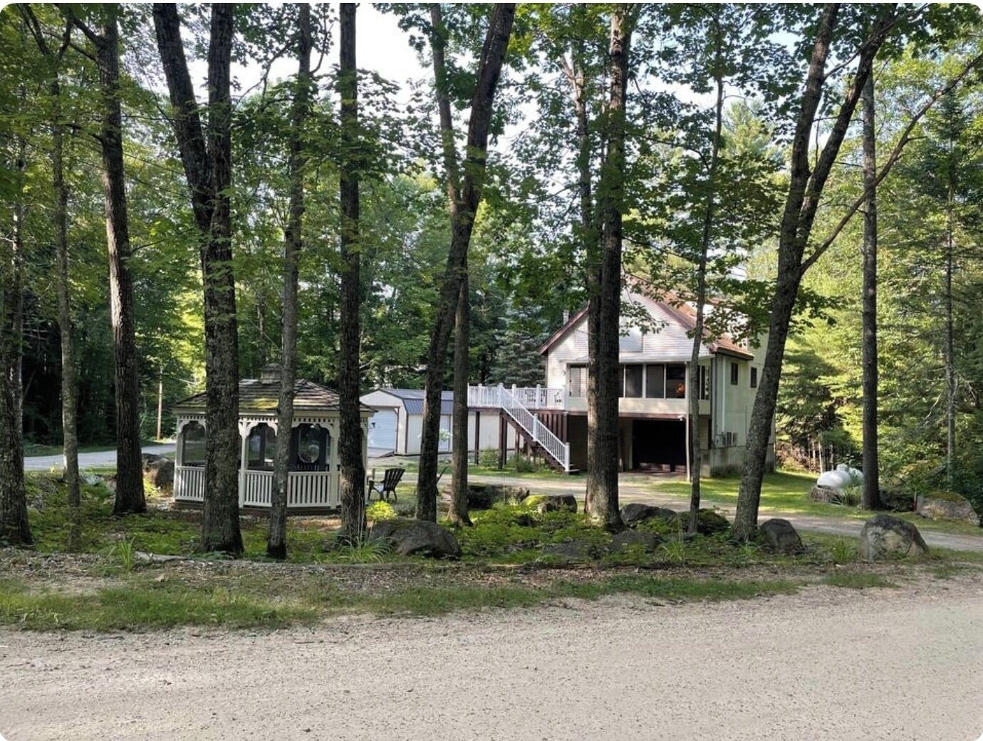 Une maison à deux étages dotée d’un porche couvert et d’un garage, entourée de grands arbres et bordée d’une allée en gravier.
