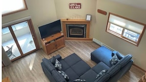 Una sala de estar con sofá, televisión, chimenea y un cartel que dice 'La vida es mejor en el lago'.