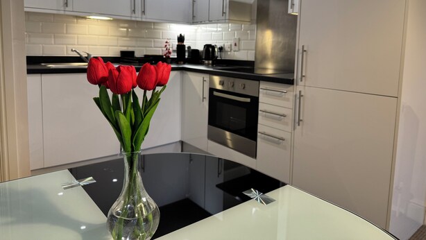 Eine moderne Küche mit weißen Schränken, einer Edelstahl-Dunstabzugshaube und einem Glastisch mit einer Vase roter Tulpen.