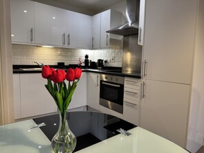 A modern kitchen with white cabinets, a stainless steel range hood, and a glass table with a vase of red tulips.