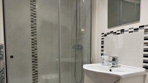 Ein modernes Badezimmer mit einer Glaskabine zur Dusche, einem weißen Waschbecken und einer gefliesten Rückwand.