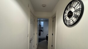 Ein Korridor mit einer großen Wanduhr, weißen Türen und einem Teppichboden, der zu einer Küche führt.
