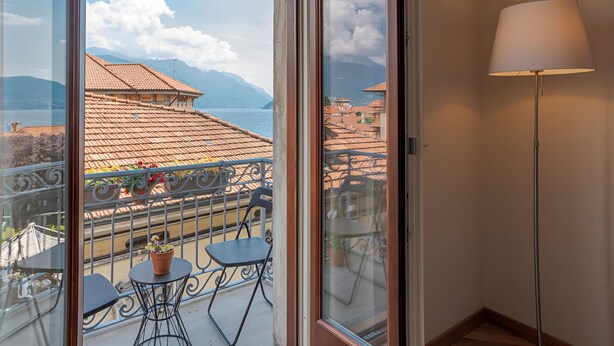 Un balcon avec vue sur les montagnes et un lac, une plante en pot et une table avec des chaises.
