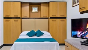 Habitación de hotel con cama, televisión, armarios de madera y un pequeño cuadro en la pared.
