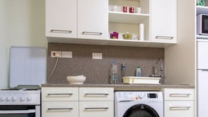 Una cocina compacta con armarios blancos, estufa, lavadora y microondas.