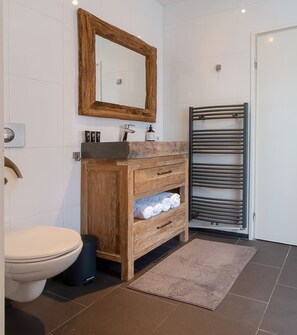 Een moderne badkamer met een houten wastafelmeubel, een grote spiegel, een handdoekrek en een toilet.