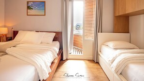 Habitación de hotel con dos camas, piso de madera, un cuadro de playa y vistas a través de una puerta.