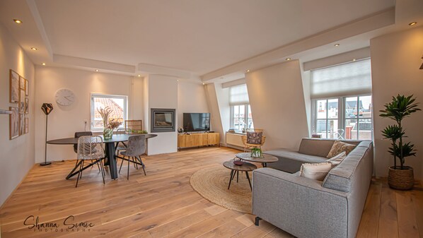 Een moderne woonkamer met een eethoek, een bank, een televisie en grote ramen.