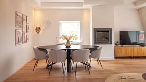 Una sala de estar moderna con una mesa redonda de comedor, sillas grises, una chimenea y un televisor.
