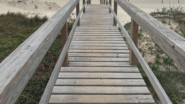 Une promenade en bois qui mène à une plage, avec des vagues en arrière-plan.