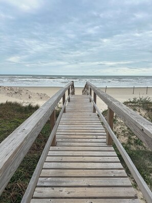 A wooden boardwalk leading to a beach with waves in the background.