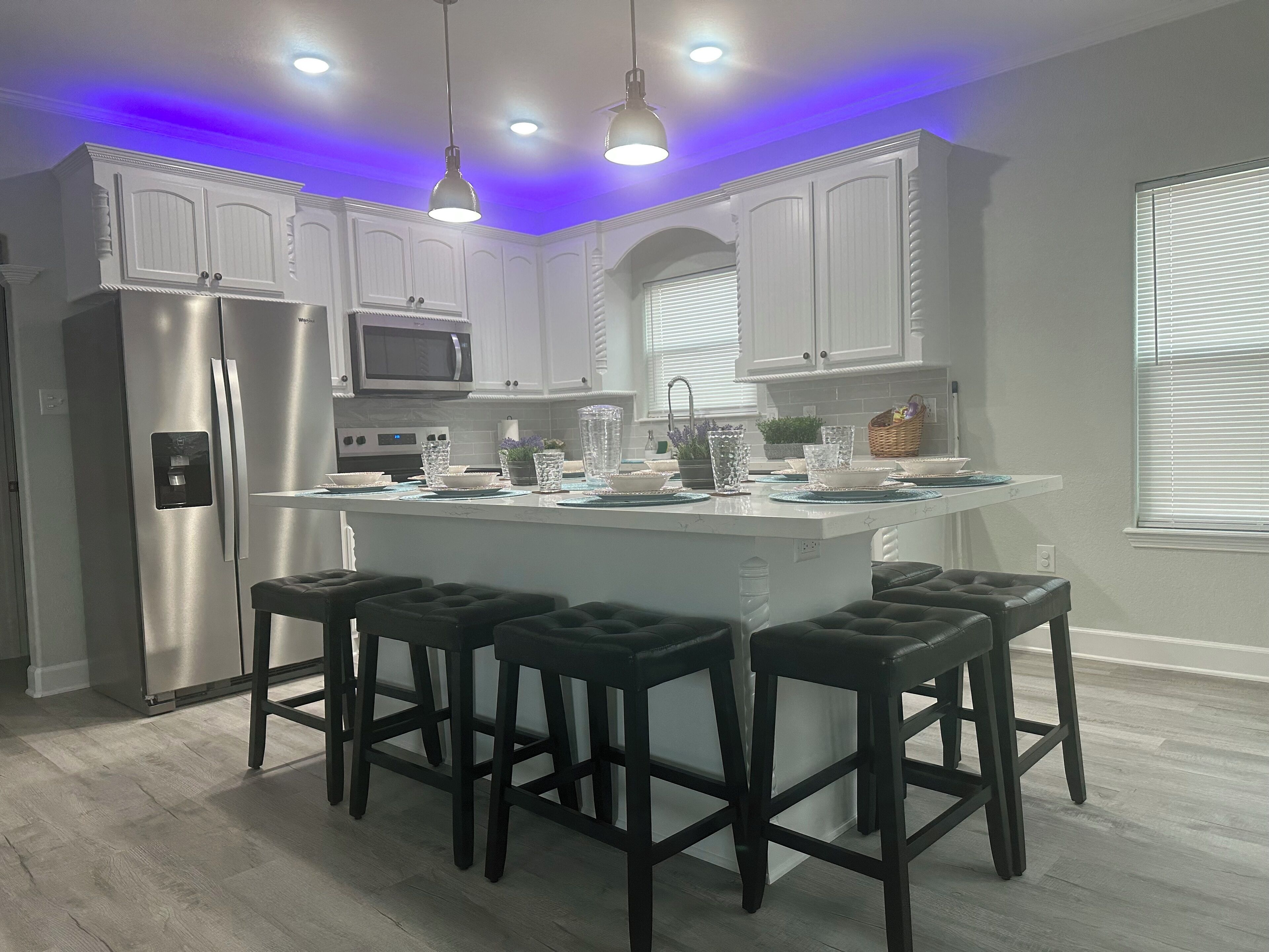 A modern kitchen with white cabinetry, a central island with bar stools, stainless steel appliances, and pendant lighting.