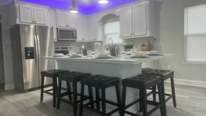 Une cuisine moderne avec des meubles blancs, un îlot central doté de tabourets, des appareils en acier inoxydable et un éclairage suspendu.