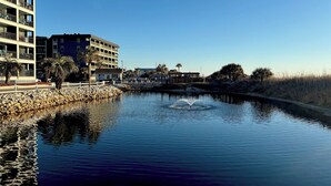A calm water body with a fountain, surrounded by a white fence and palm trees. - Ocean and sunrise views that have you coming back year after year! (Myrtle Beach)