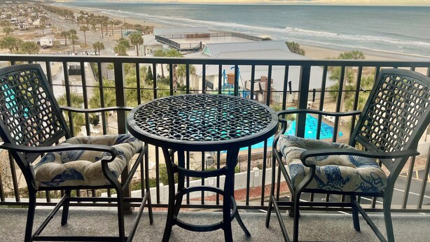 A balcony with a table and two chairs, overlooking a beach and ocean. - Ocean and sunrise views that have you coming back year after year! (Myrtle Beach)