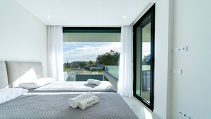 A modern hotel room with two beds, a large sliding glass door to a balcony, and a view of the cityscape. - Villa Marina - 33 by HelloVacations (Albufeira)