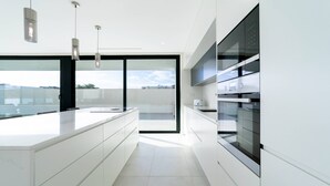A modern kitchen with a large island, built-in appliances, and a view through the glass door. - Villa Marina - 33 by HelloVacations (Albufeira)