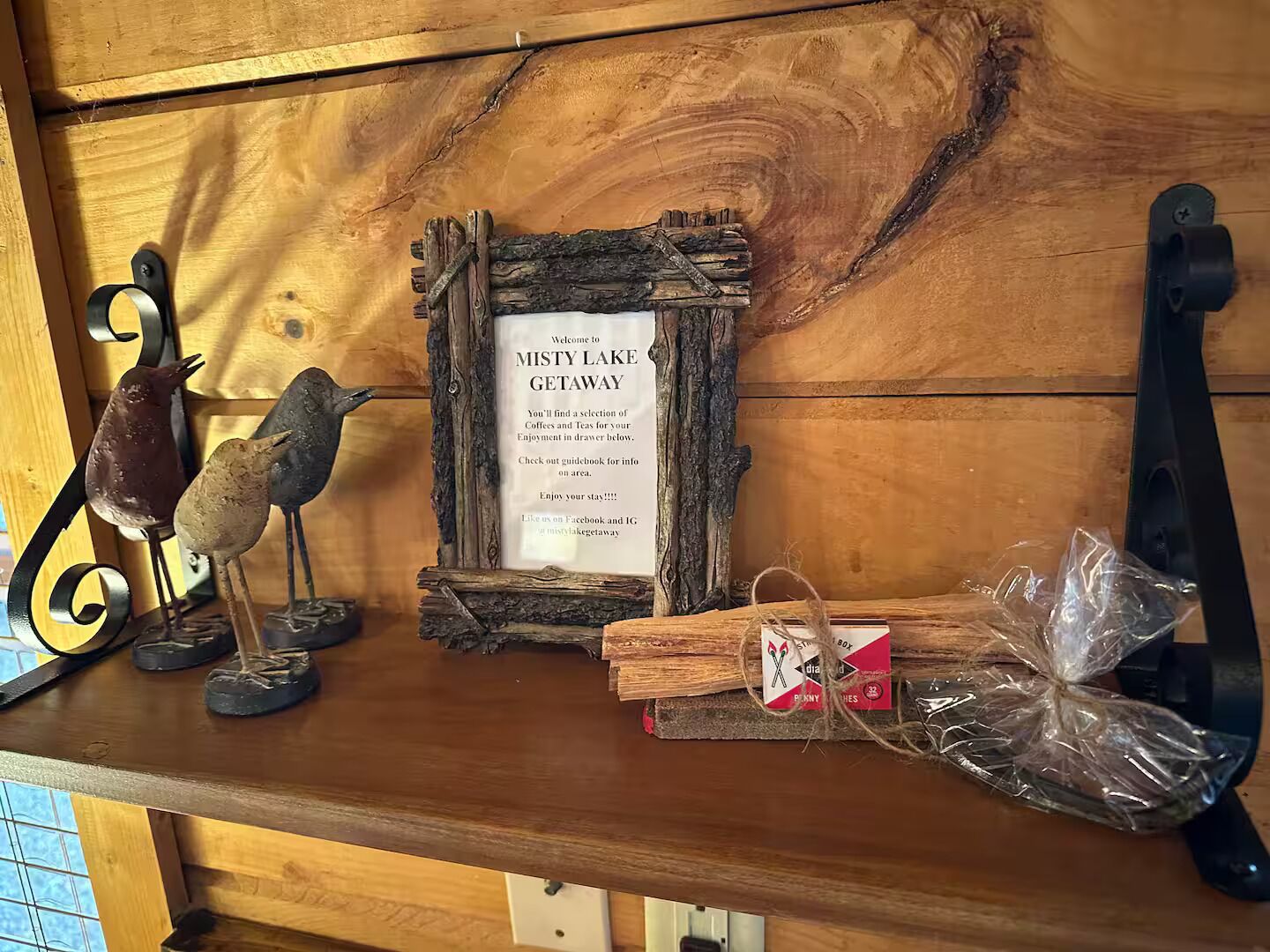 A wooden shelf with a rustic sign reading "Misty Lake Getaway," a decorative bird sculpture, and a small gift box tied with twine.