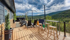 Um deck de madeira com móveis para área externa, espaço para churrasco e vista panorâmica das montanhas.