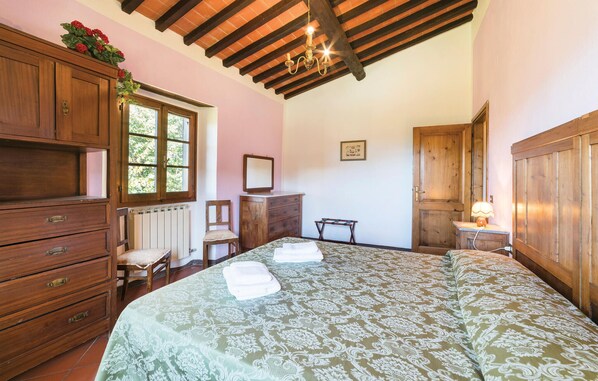 Un dormitorio con una cama grande, muebles de madera, un radiador, una ventana y una araña.