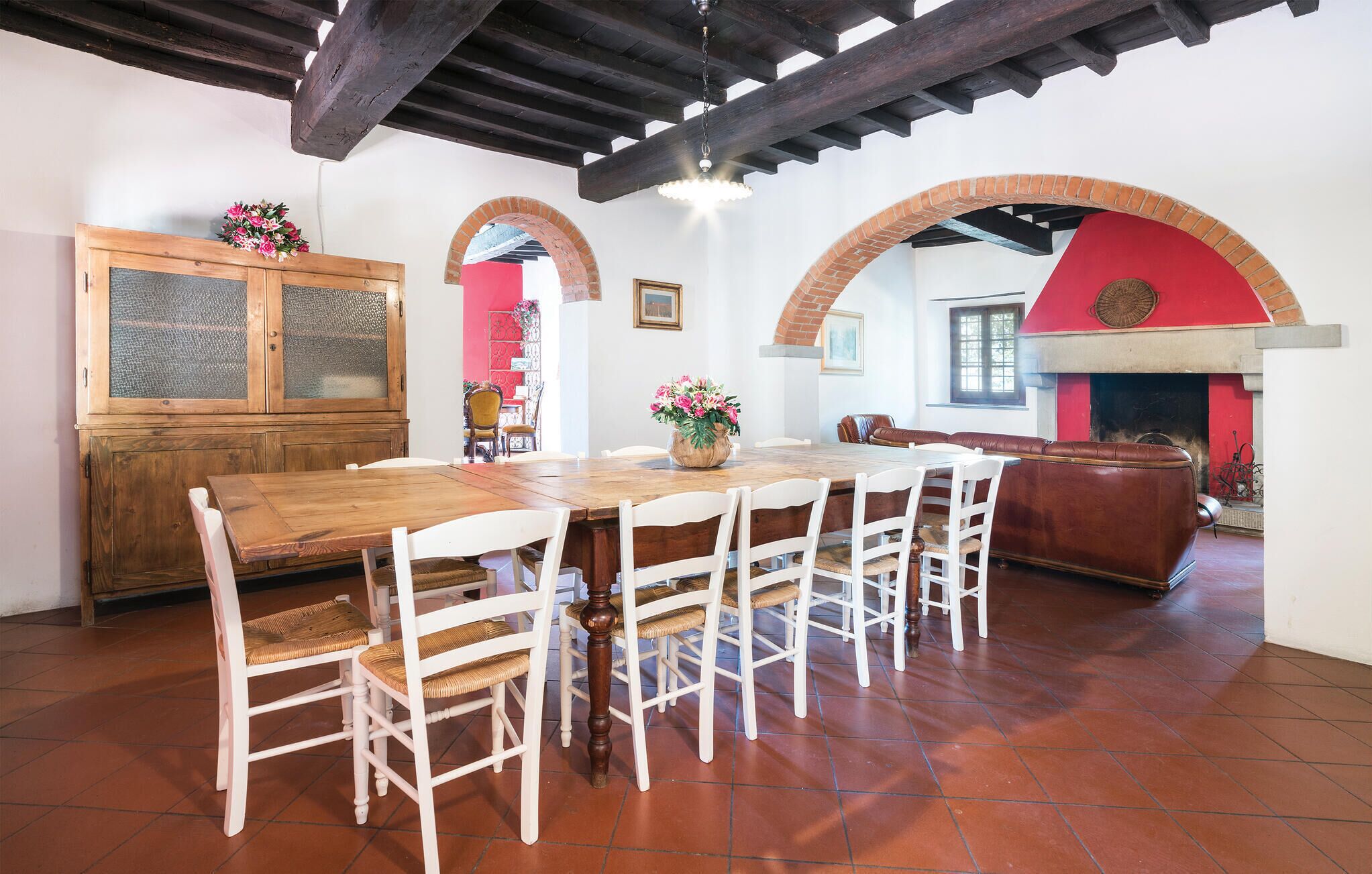 Zona pranzo con tavolo in legno e sedie bianche, un armadietto in legno e un camino in mattoni rossi.