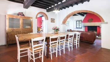 Zona pranzo con tavolo in legno e sedie bianche, un armadietto in legno e un camino in mattoni rossi.