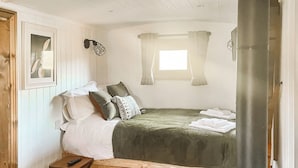 Un dormitorio acogedor con cama, almohadas, una mesita y una ventana con cortinas.
