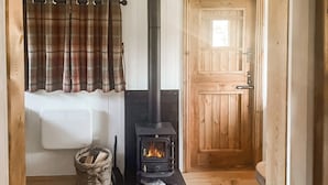 Una habitación acogedora con una estufa de leña, una cesta de mimbre y una cortina a cuadros.