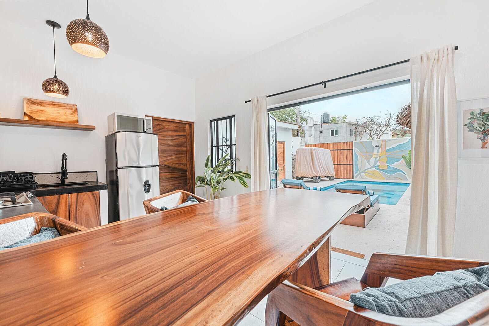 A modern kitchen with a wooden dining table, a refrigerator, and pendant lights.