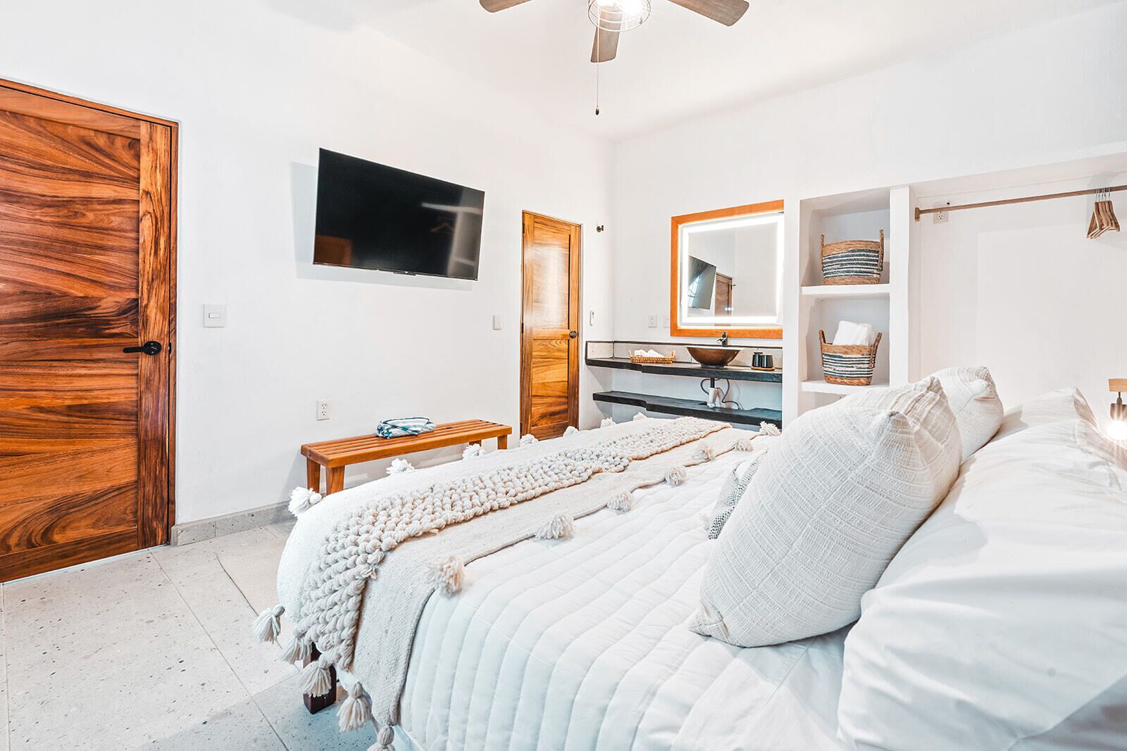 A bedroom with a bed, a wooden door, a television, a mirror, and a shelf with baskets.