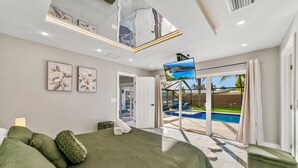 A modern bedroom with a large bed, a flat-screen TV, and a view of a swimming pool through glass doors.