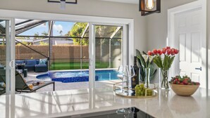 Une cuisine moderne dotée d’un grand îlot central, un coin repas avec vue sur la piscine et un espace salon confortable également avec vue sur la piscine.