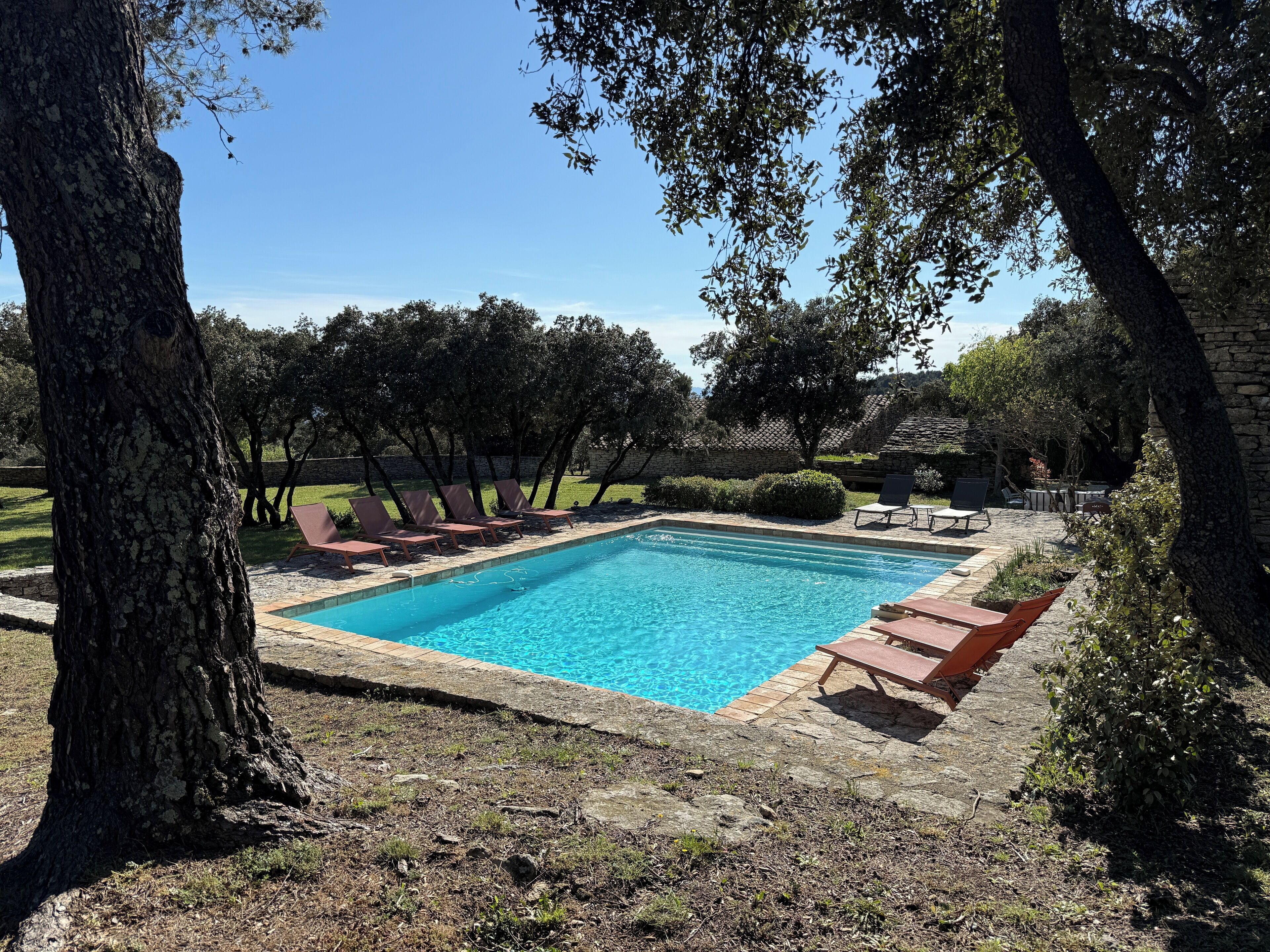 A rectangular swimming pool with a stone border, surrounded by lounge chairs and a stone wall.